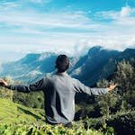 A man with open arms enjoying the breathtaking view of Munnar's lush tea plantations and majestic mountains.