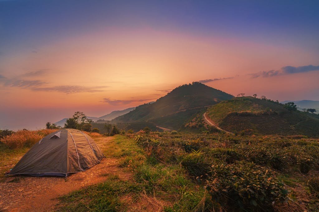 Explore a tranquil mountain campsite with a tent under a vibrant sunrise sky.
